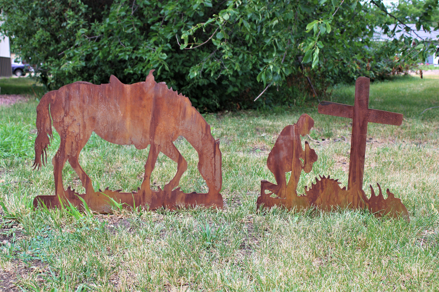 Rusty metal praying cowboy kneeling in front of a cross with a horse