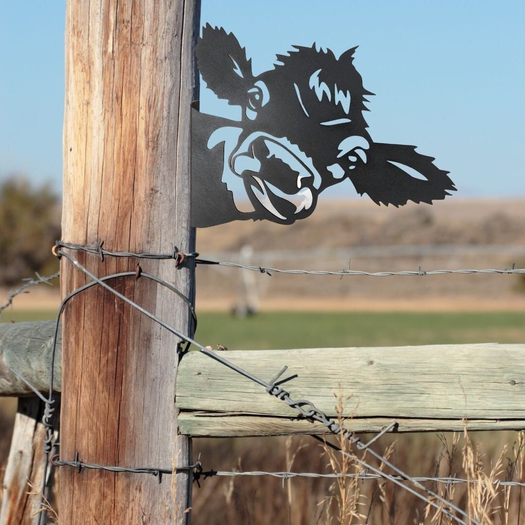 Black powder coat metal cow head peeking around a tree