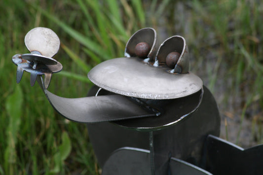 Raw steel metal frog statue with an outstretched tongue and fly