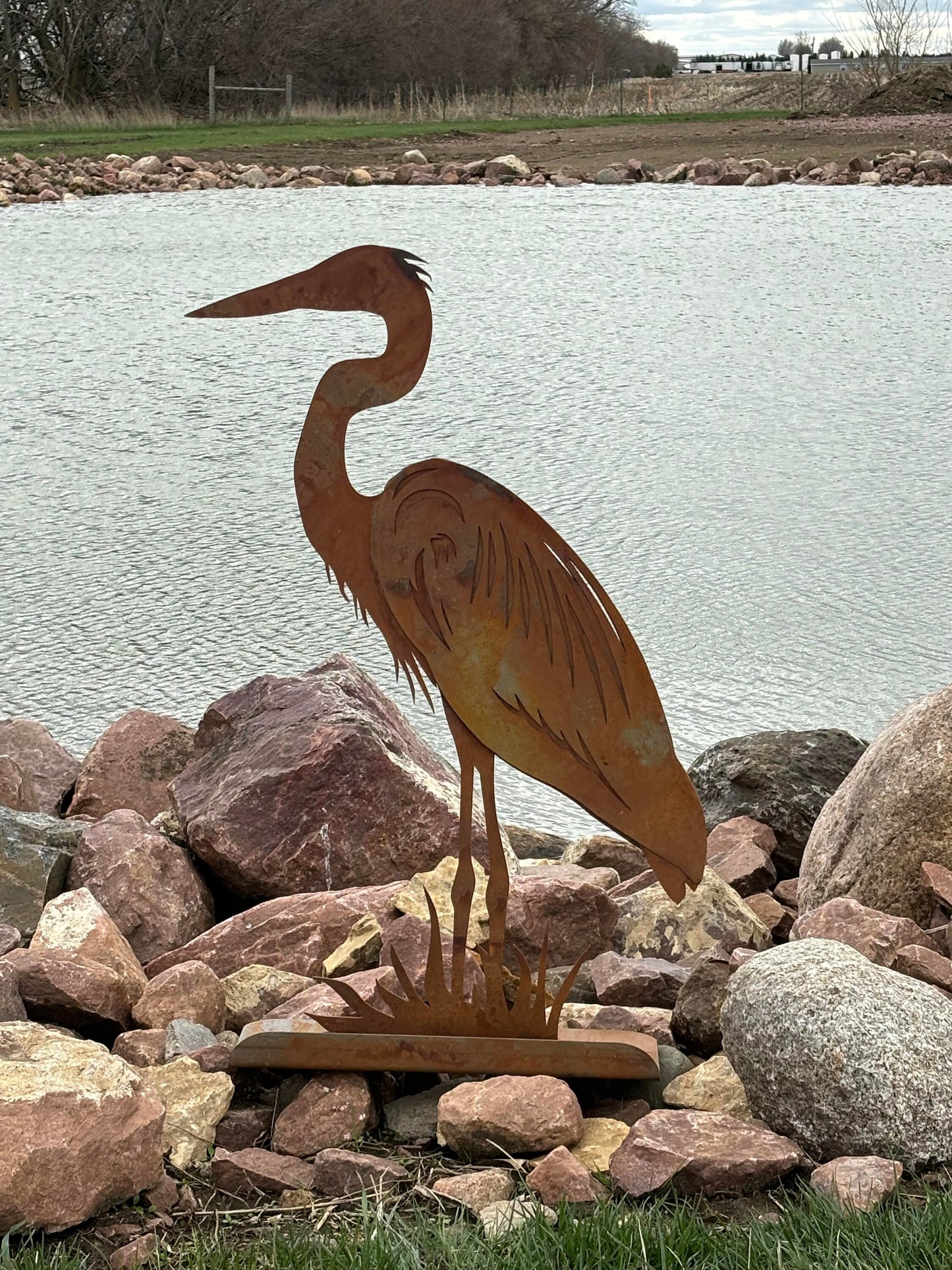 Rusty metal heron statue in front of a pond