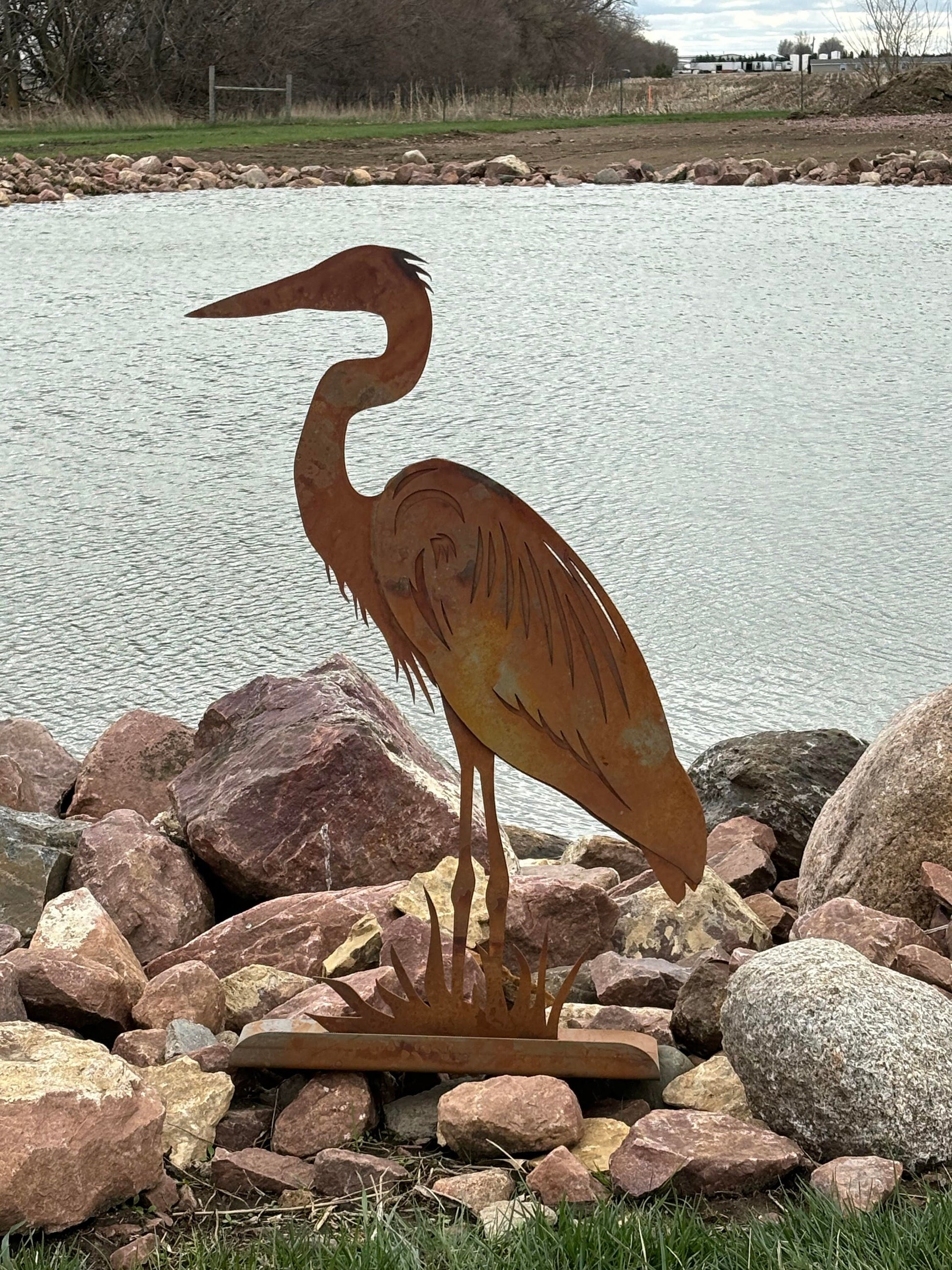 Rusty metal heron statue in front of a pond