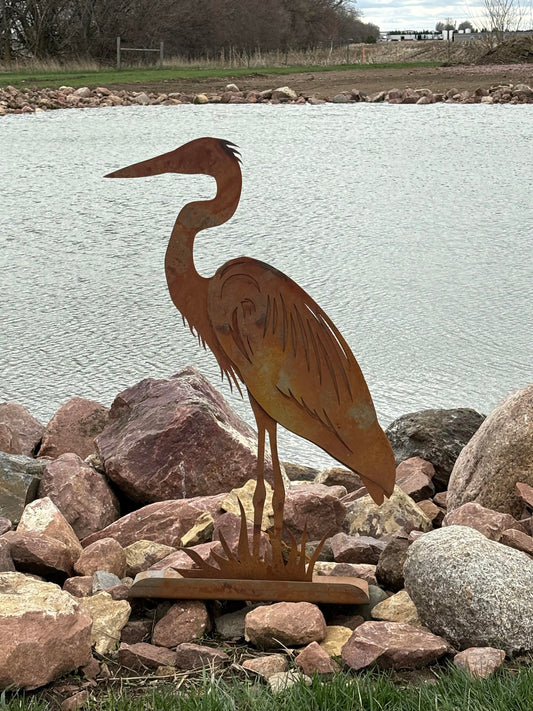Rusty metal heron statue in front of a pond